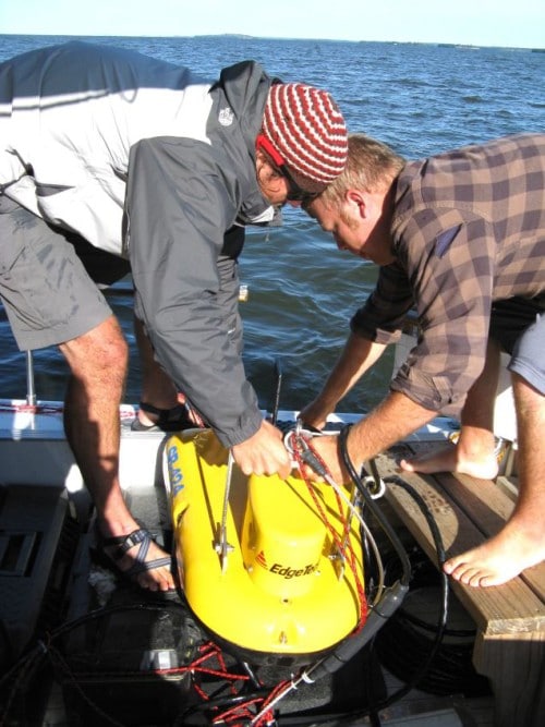 Devin Hougardy and Aaron DeRusha deploy the towfish used to take seismic profiles of the lake bottom. (Photo by Mark Edlund)