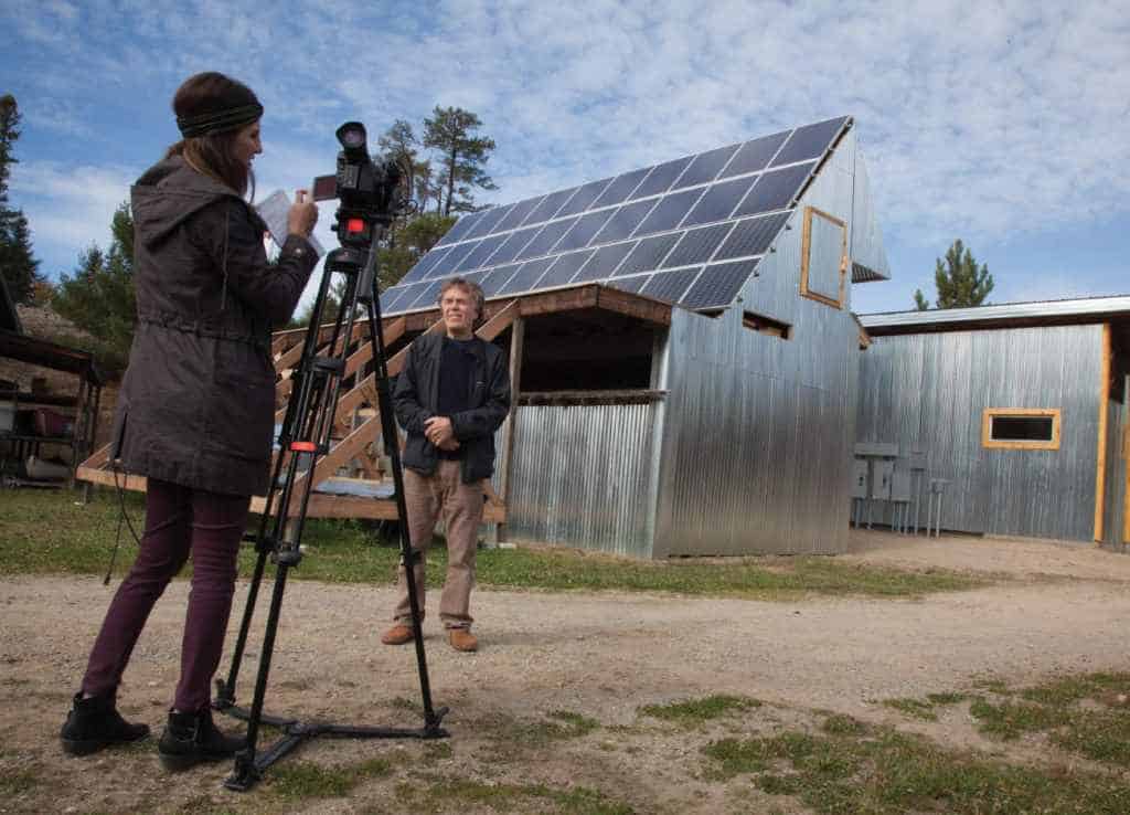 Polar explorer Will Steger being interviewed and photographed by media in front of the newly installed solar array at the Steger Wilderness Center. This is the first micro-grid up and running in Minnesota. Photo by John Ratzloff.