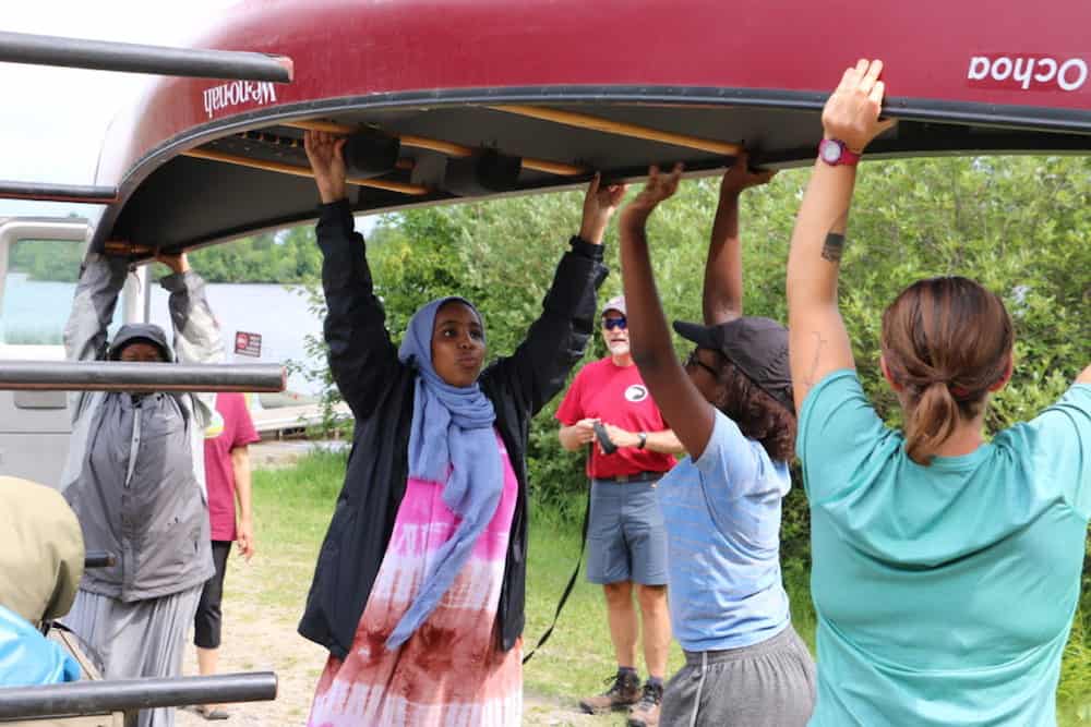 Young women with Sisterhood Boutique work together to lift a canoe. 