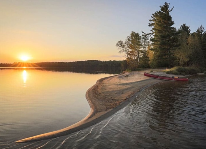 canoe on beach in Quetico with sunset over lake