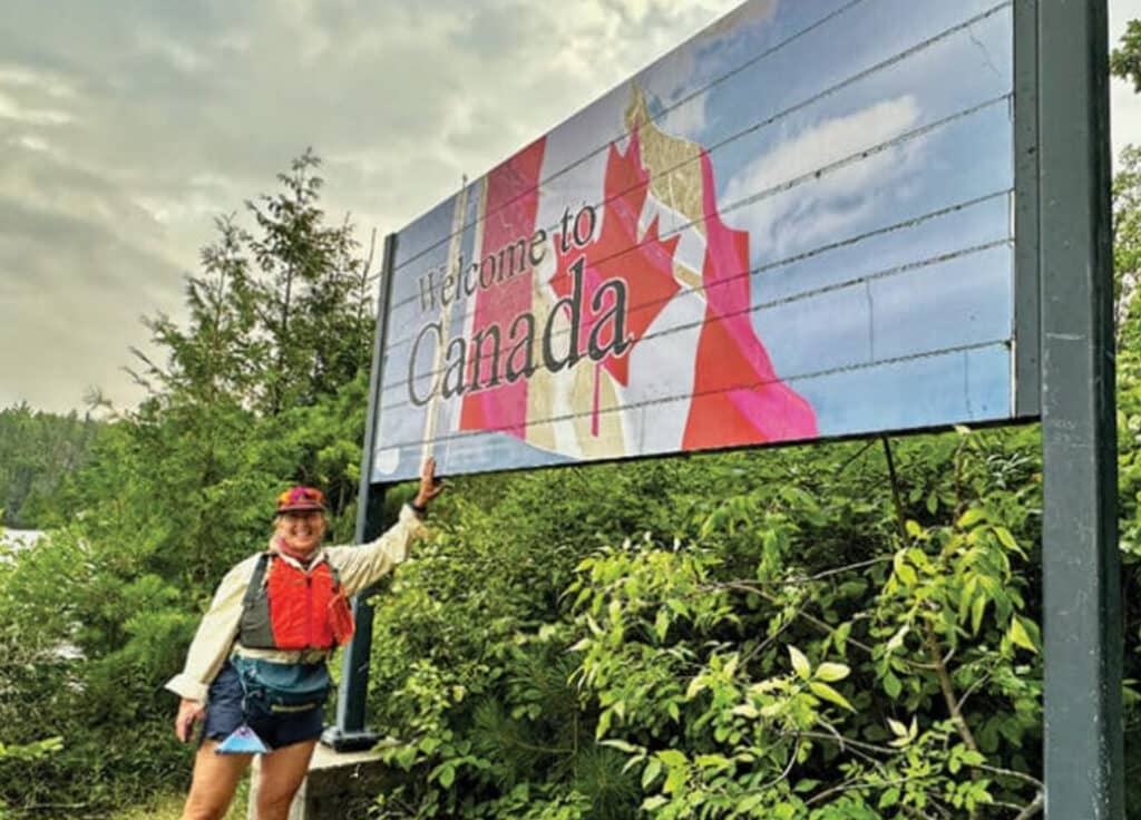 paddler stands by welcome to Canada sign at Quetico park lake