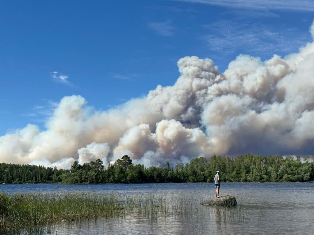 A person stands on a rock and watches smoke billowing over Boundary Waters from the Camp Fire near Ely