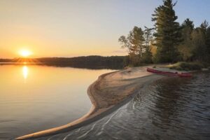 canoe on beach in Quetico with sunset over lake