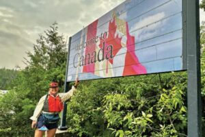 paddler stands by welcome to Canada sign at Quetico park lake