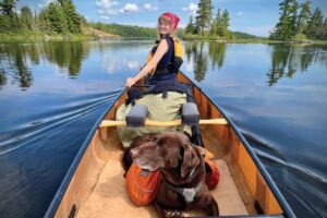 girl paddling and looking back at a dog in a canoe